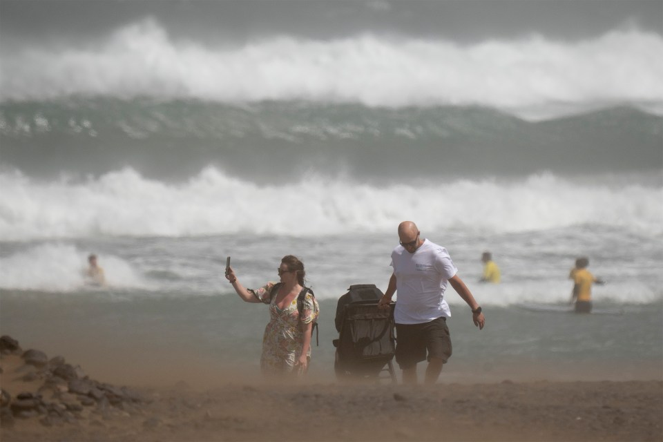 Tourists on a beach with large waves during a storm.