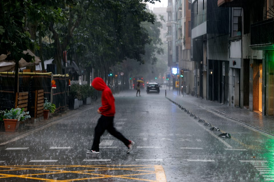 Person crossing a rain-soaked street in Barcelona.