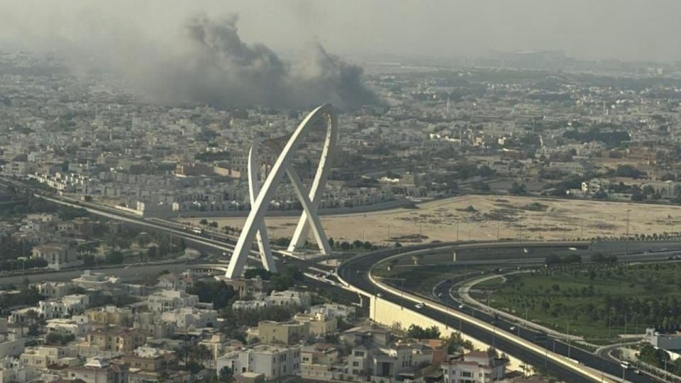 Smoke rising over Doha, Qatar, near a bridge.