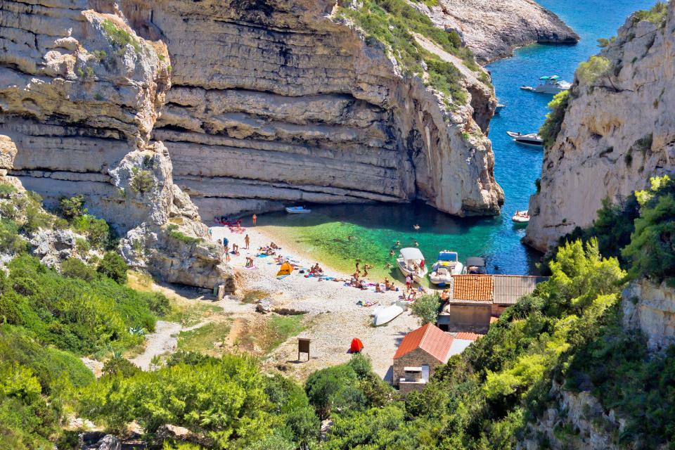 Stinva Bay beach on Vis Island, Croatia, with boats and people swimming and sunbathing.