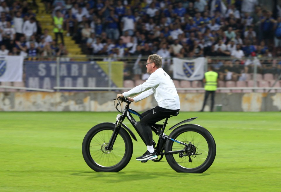 Ralf Rangnick riding a bike on a soccer field.