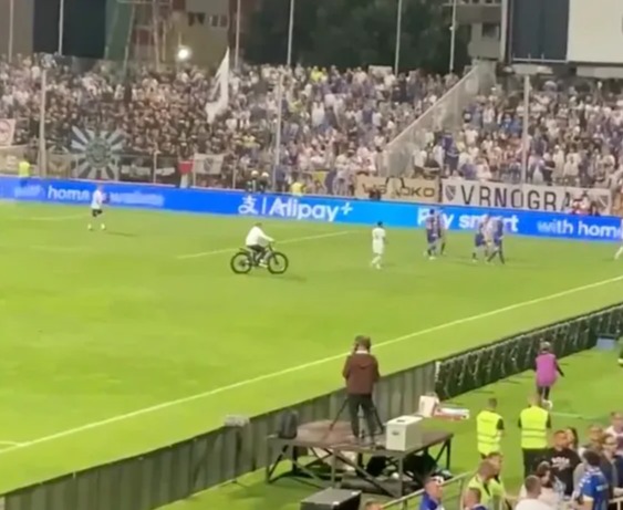 Person on a bicycle riding across a soccer field during a game.