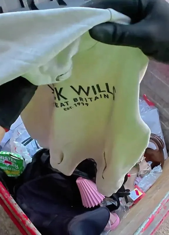 A person holding up a beige sweatshirt with "Jack Wills Great Britain Est. 1999" printed on it, found in a dumpster.