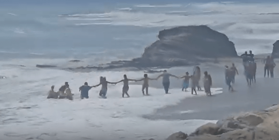 Human chain rescuing a boy from strong currents at a beach.