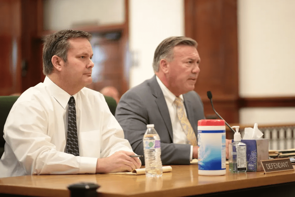 Two men sitting at a table during a hearing.