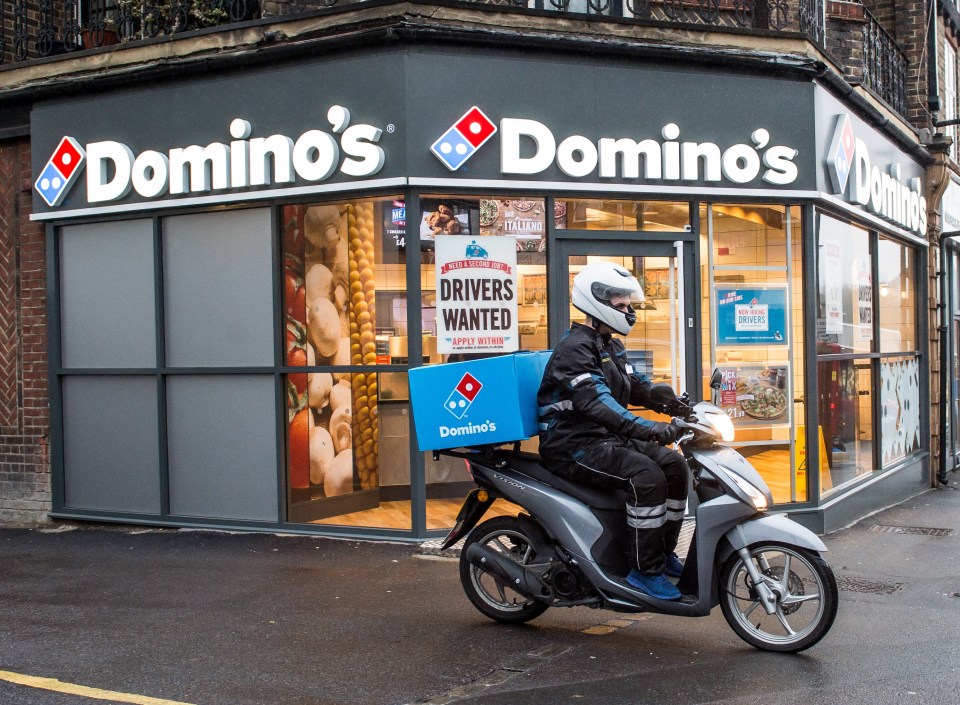 Domino's Pizza delivery driver on scooter outside store.
