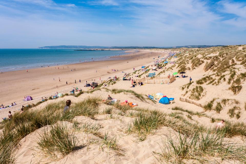 Crowded beach with sand dunes.