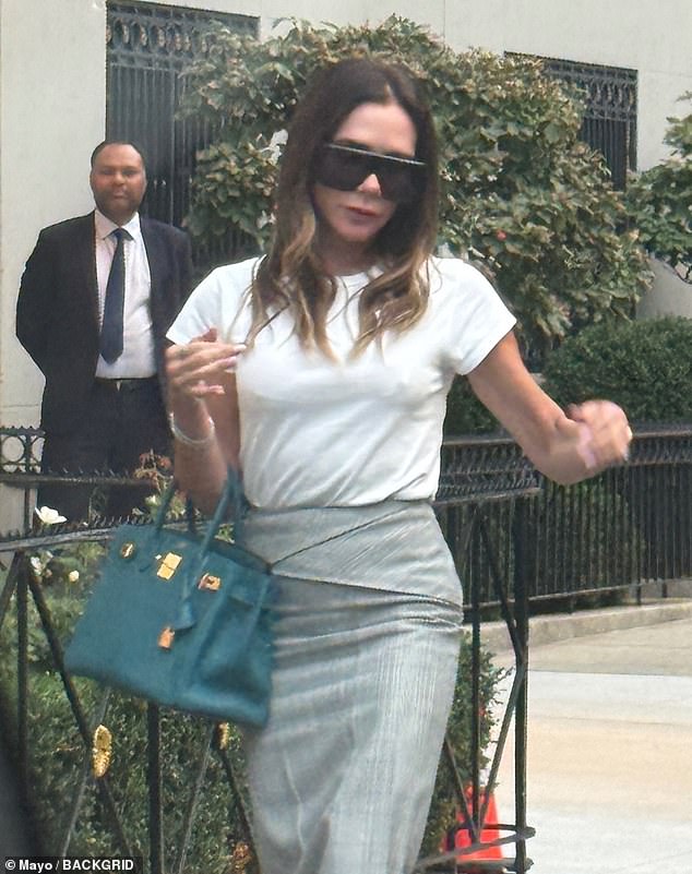 The Spice Girl turned fashion designer, 51, wore a crumpled top tucked into a grey midi skirt, while completing the look with bold red heels