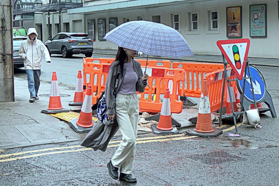 Woman with umbrella walking past street construction in Glasgow, Scotland.