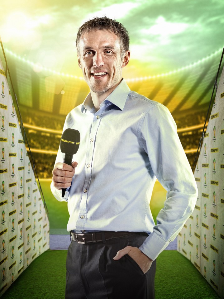 Phil Neville holding a microphone in front of a soccer stadium backdrop.