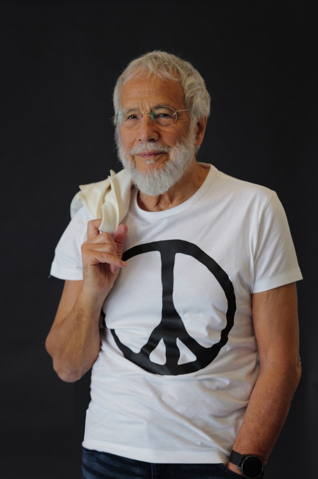 Portrait of Yusuf Islam (Cat Stevens) wearing a white t-shirt with a peace symbol.