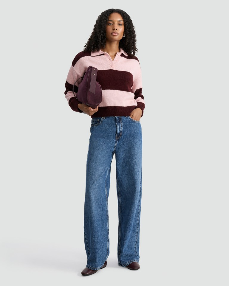 Woman in striped sweater, jeans, and burgundy shoes holding a bag.