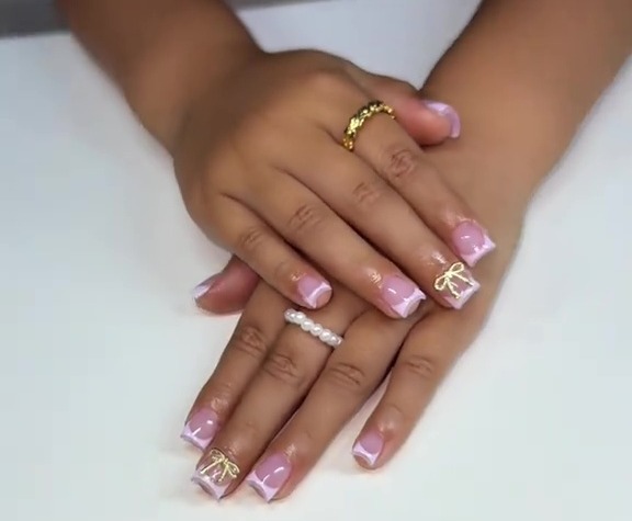 Child's hands with light purple and white nail polish and gold bow accents.