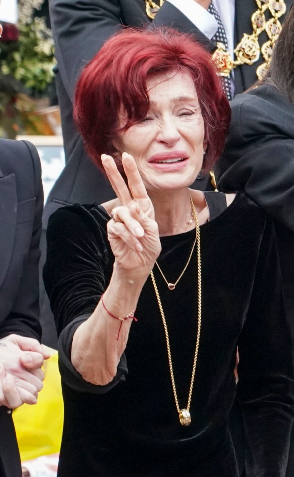 Sharon Osbourne crying and giving a peace sign.