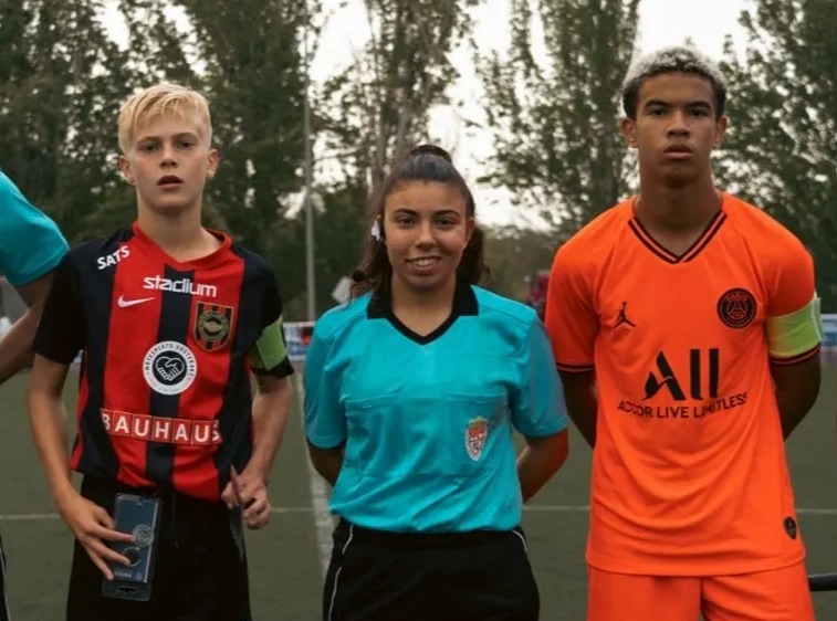 Four young soccer referees and a player standing on a field.