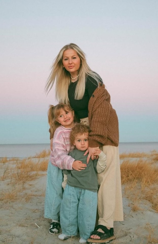 A mother and her two young children stand on a beach.