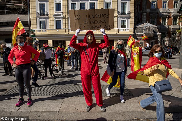 A demonstrator dressed in the iconic 'La Casa the Papel' (Money Heist) red jumpsuit holds a placard reading 'Should we call it dictatorship, or not yet?' during an protest against the Spanish government on October 12, 2020 in Madrid, Spain