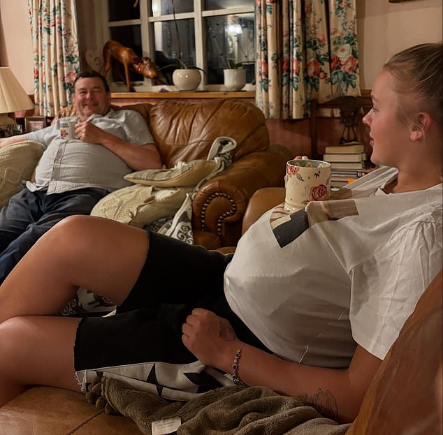 JoJo and potential father-in-law Paul on adjacent leather sofas, her with a cushion stuffed inside her t-shirt and a cup of tea resting on the resulting paunch, mirroring his pose