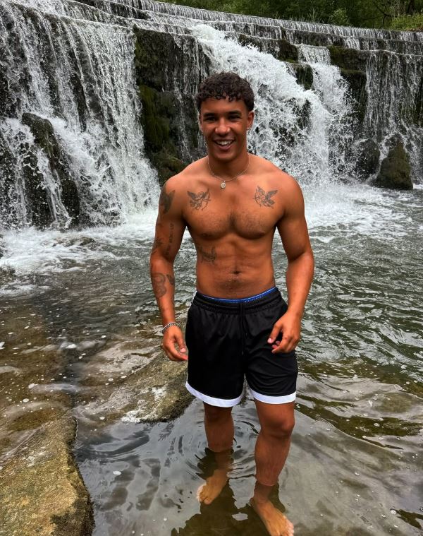 Man smiling in shallow water in front of a waterfall.