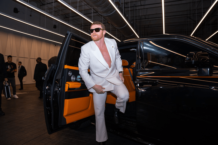 Man in white suit exiting a black car.
