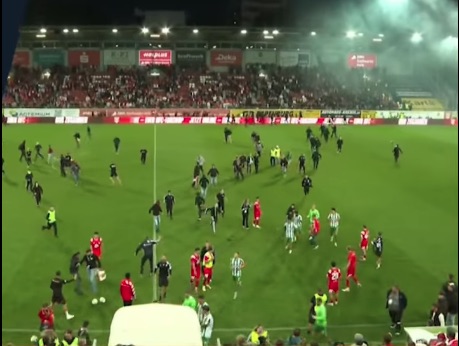 Soccer game interrupted by fans running onto the field.