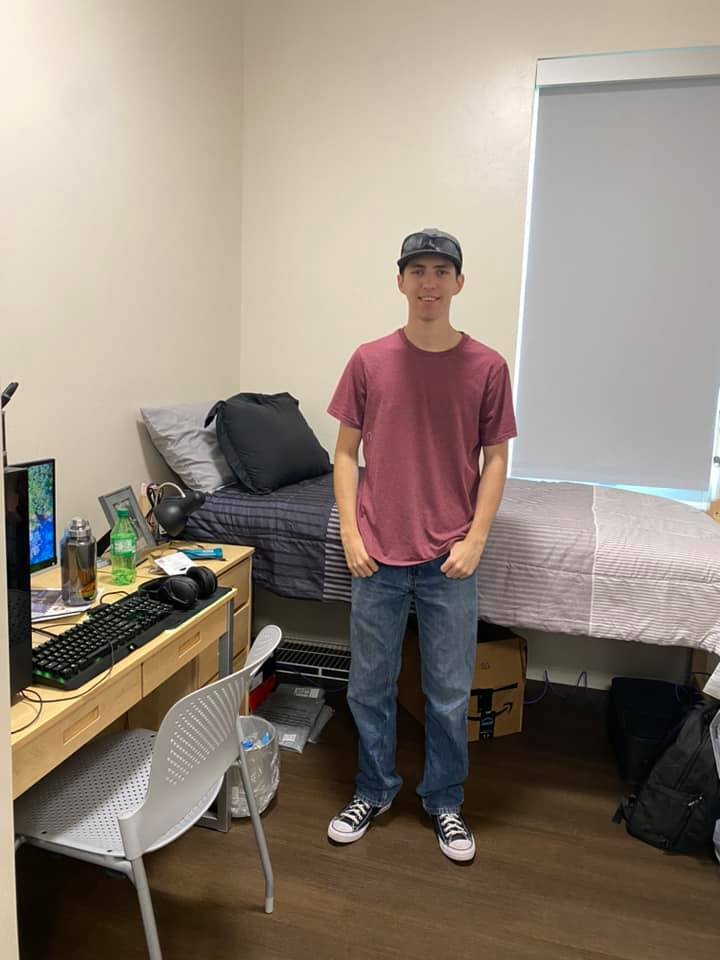 A young man standing in his dorm room.