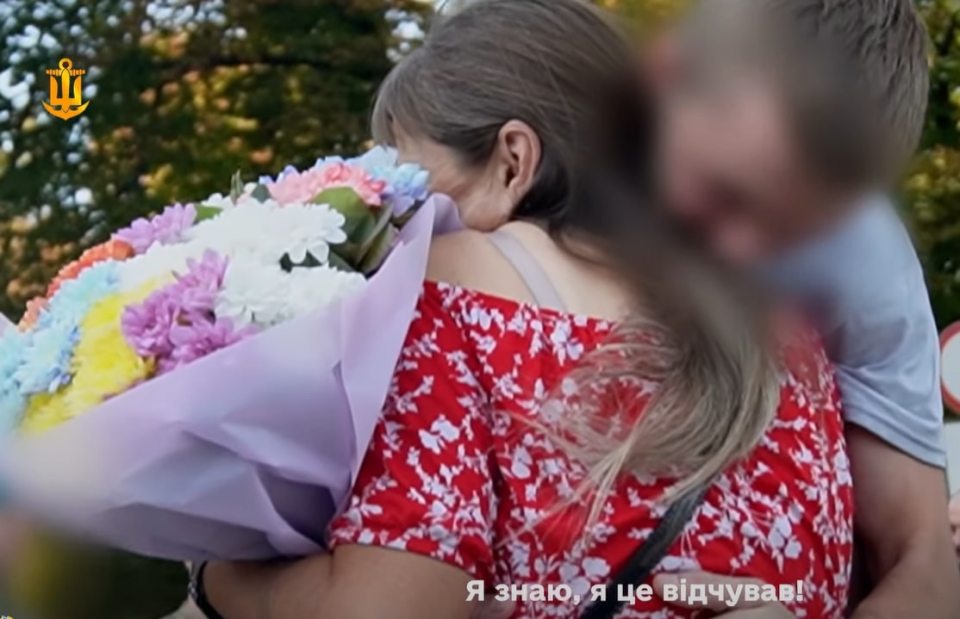 Woman embracing a person, holding a bouquet of flowers.