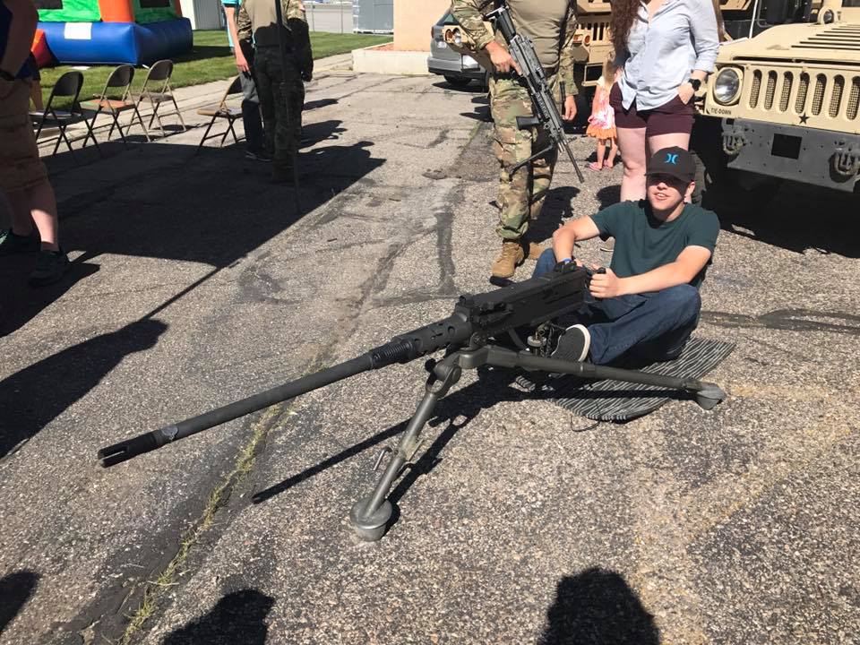 A young man sits beside a mounted machine gun.