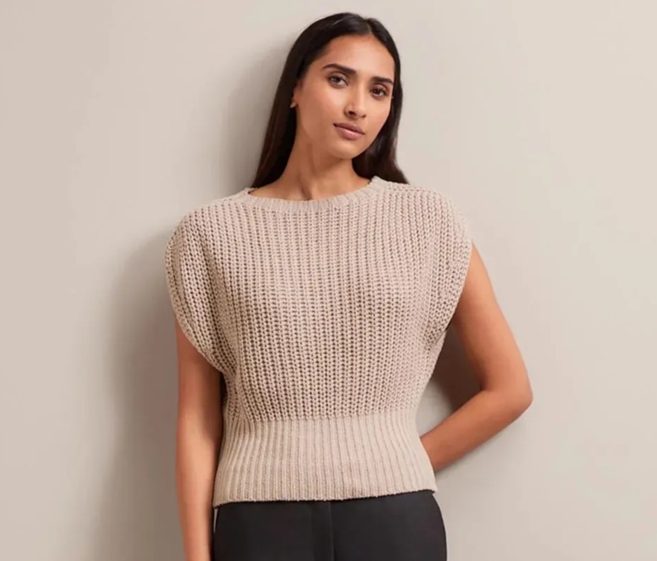 Woman wearing a beige knitted vest and black trousers.