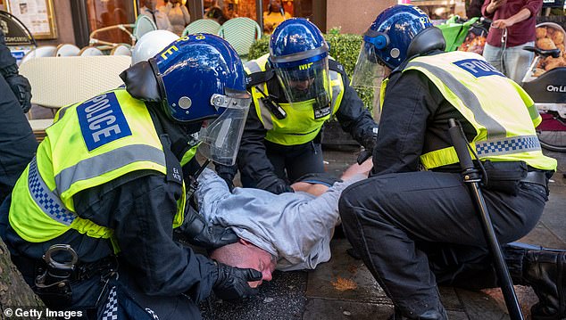 Three police officers restrain a man at the protest in London on Saturday