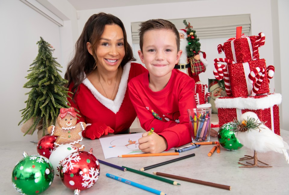 Woman and boy in Santa outfits drawing a Christmas card.