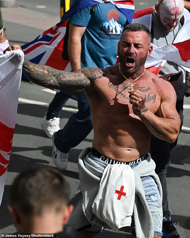 A shirtless protester attends the Unite The Kingdom protest on Saturday while brandishing an England flag and a crucifix