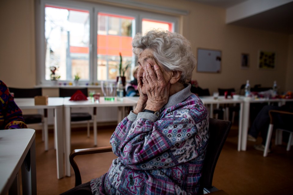 Elderly woman with her face covered by her hands in a day care facility.