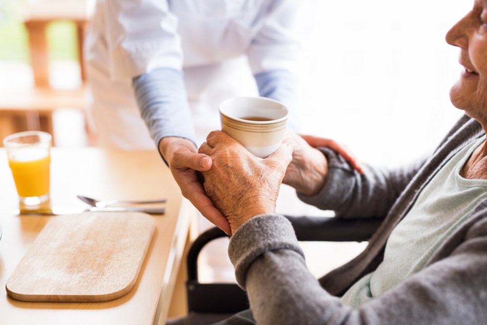 Nurse handing tea to elderly woman.