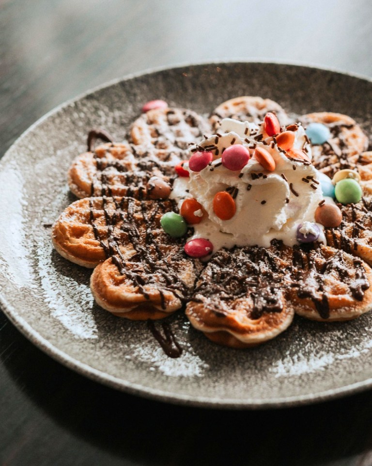 Waffles topped with whipped cream, chocolate sauce, and candy.
