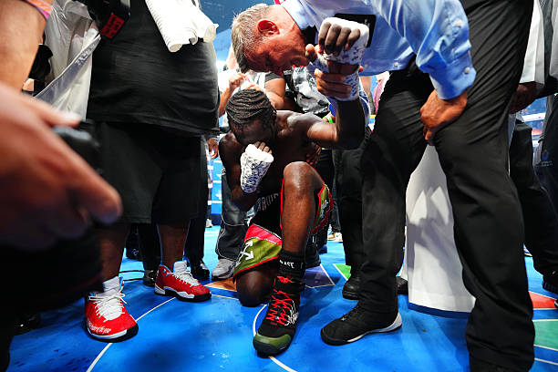 A boxer kneels, head in hands, after a fight.
