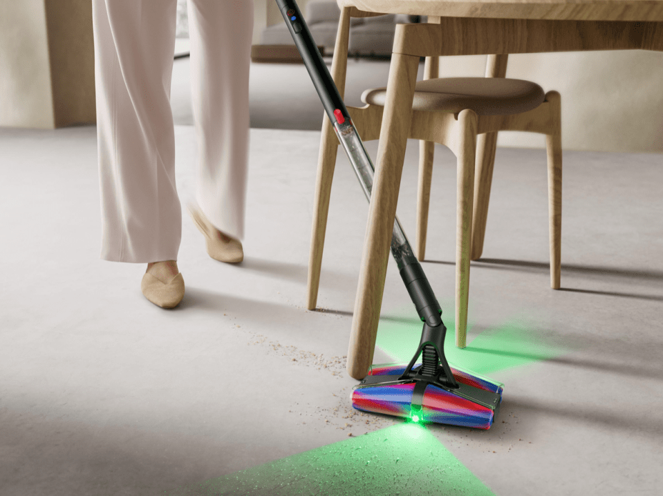 Person using a Dyson vacuum to clean under a table.