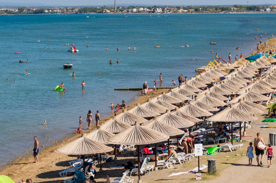 Crowded beach in Nin, Dalmatia, Croatia with many straw umbrellas.