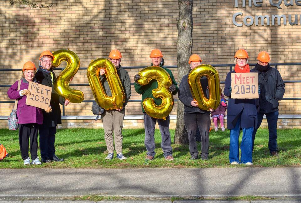 Protestors holding signs and balloons that read "Meet 2030" outside a hospital.
