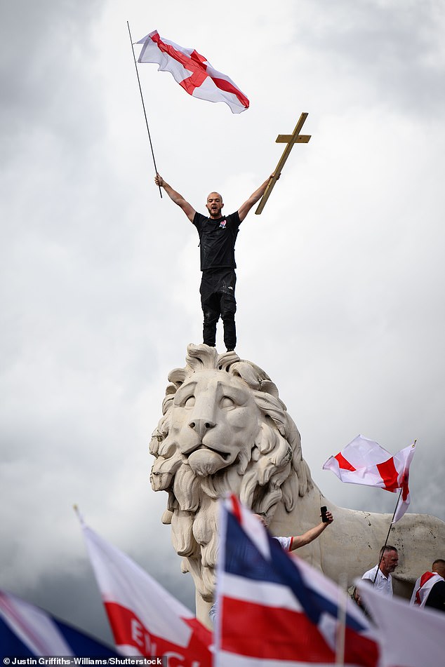 A protester at the Tommy Robinson-led march scales the South Bank Lion and holds a St George's flag and cross