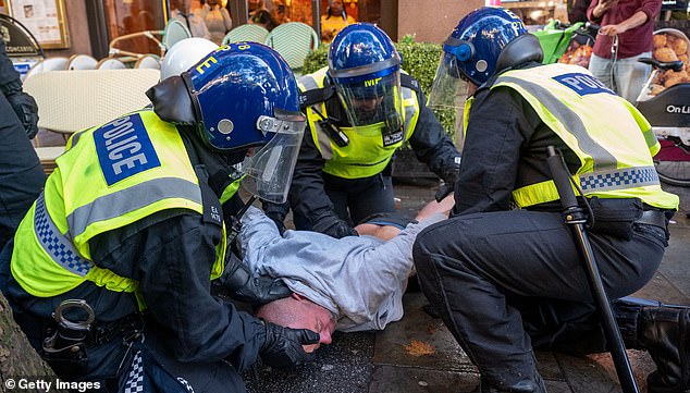 Three police officers restrain a man at the protest in London on Saturday