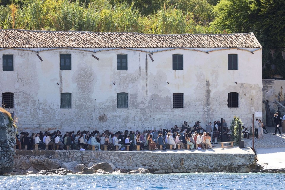 Wedding guests seated outdoors by the water during a ceremony.