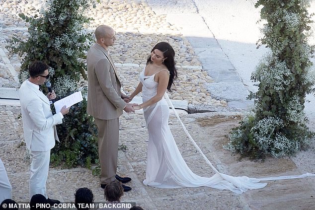 The bride's draped white dress boasted a dramatically long train that flowed behind her as she walked down the aisle and was completely sheer, revealing a figure-hugging corset underneath