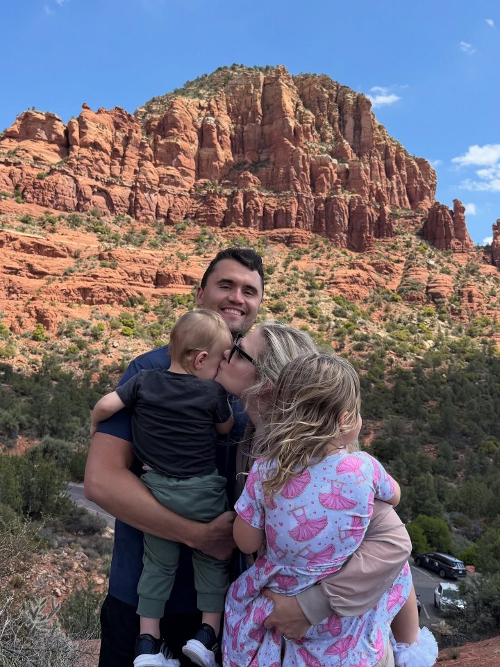 A family with two young children poses for a photo in front of red rock formations.