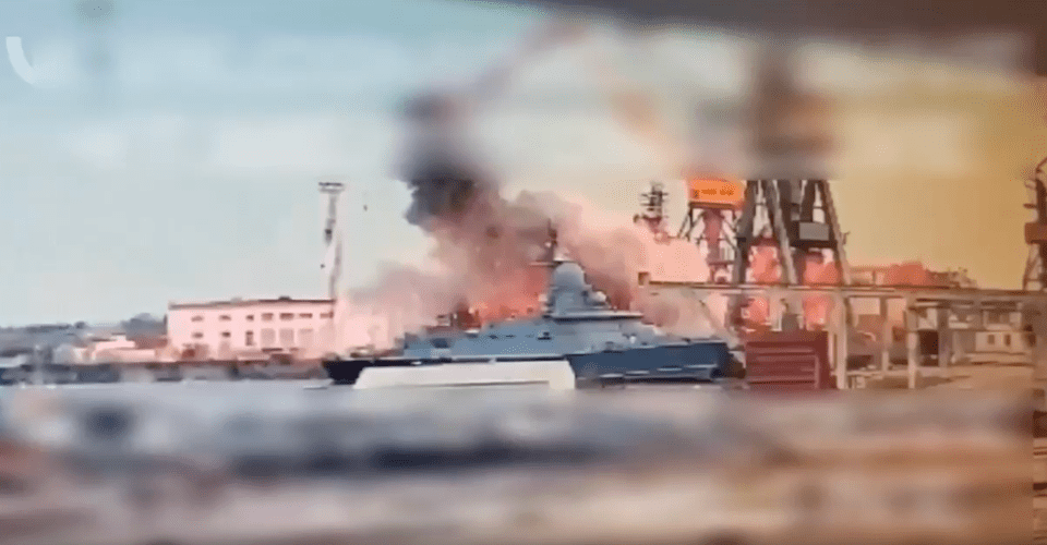 A burning ship in a harbor.