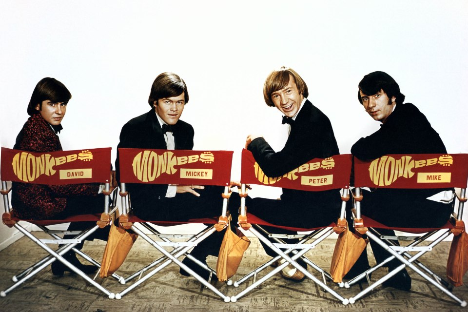 The Monkees band members Davy Jones, Mickey Dolenz, Peter Tork, and Mike Nesmith seated in director's chairs.
