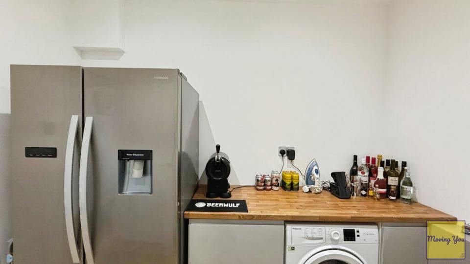 Interior view of a kitchen utility room with a toilet, refrigerator, washing machine, and various items on a countertop.