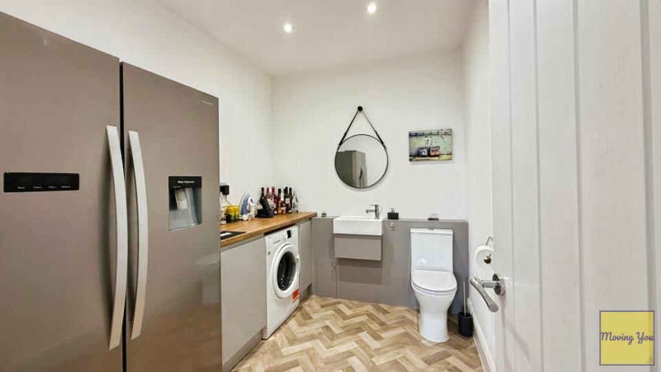 Toilet in an open-plan utility room with kitchen appliances.