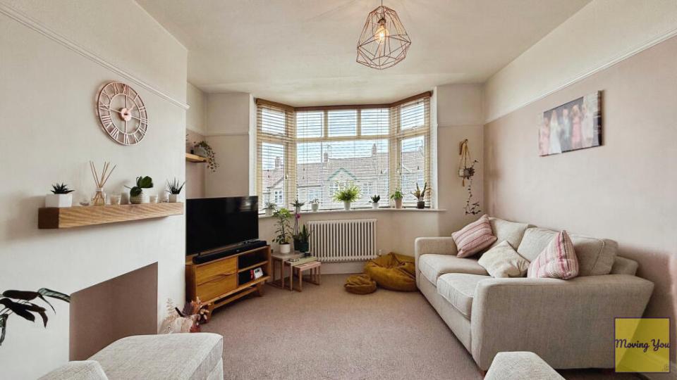Living room with beige sofa, bay window, and fireplace mantel.