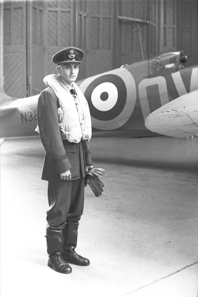 Black and white photo of a pilot in uniform standing in front of a plane.